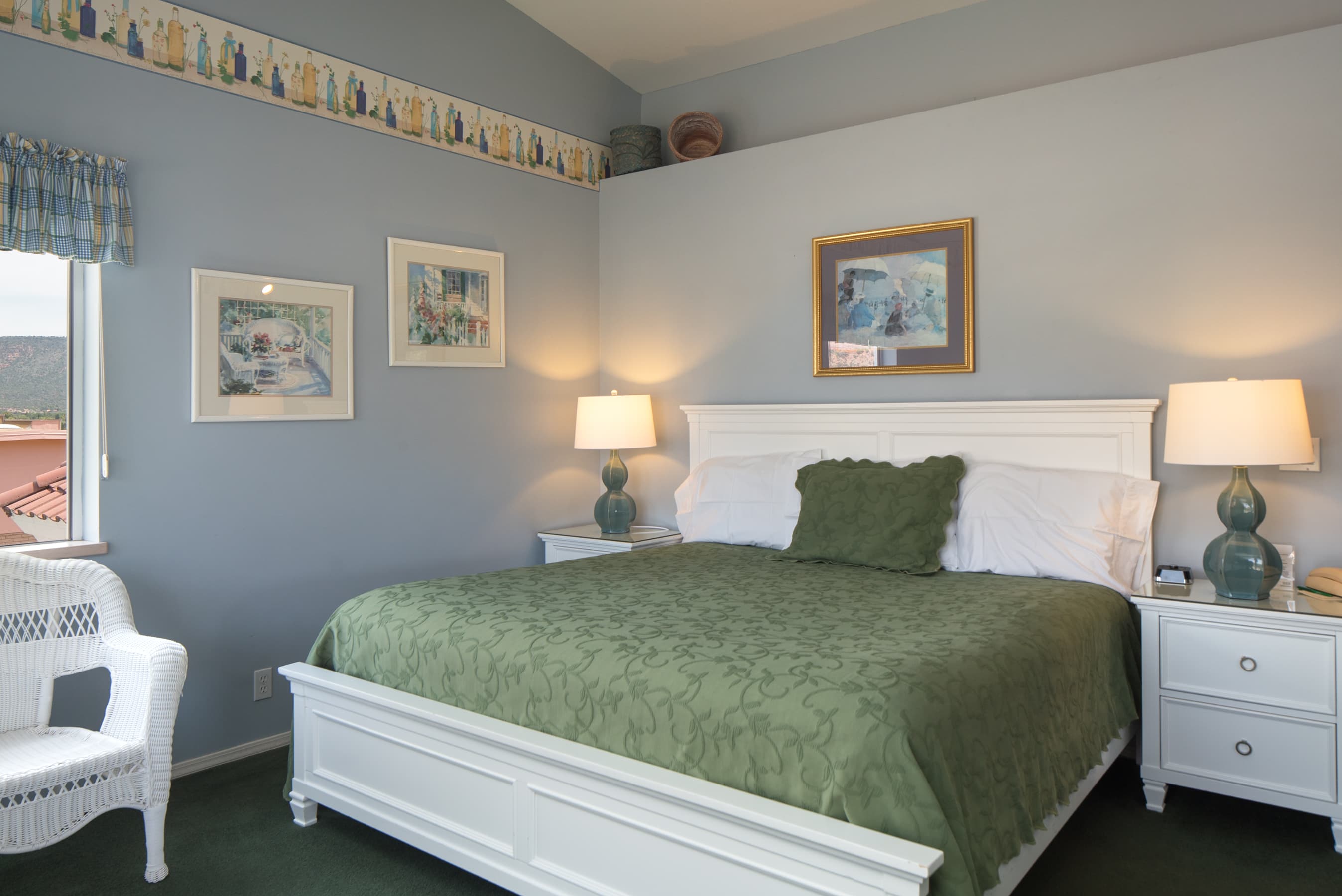 A serene bedroom with light blue walls, a white bed frame with a green comforter, two bedside tables with lamps, and a decorative border.