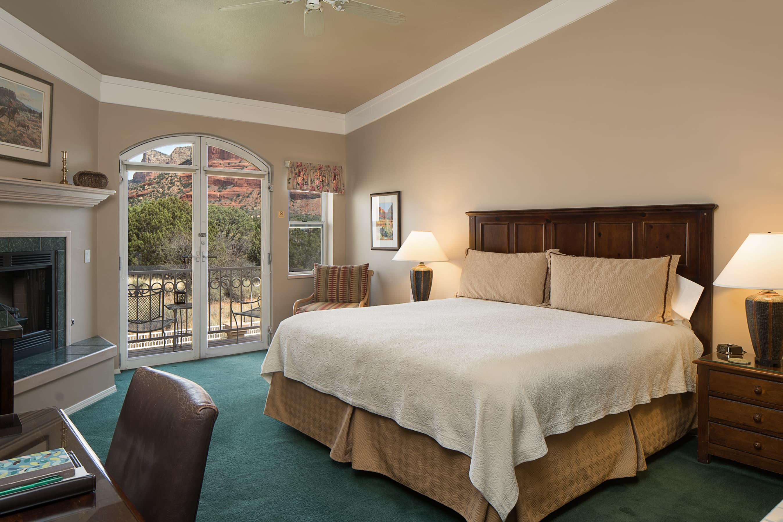 A spacious bedroom featuring a king bed, fireplace, and French doors leading to a balcony with views of vibrant red rock formations.