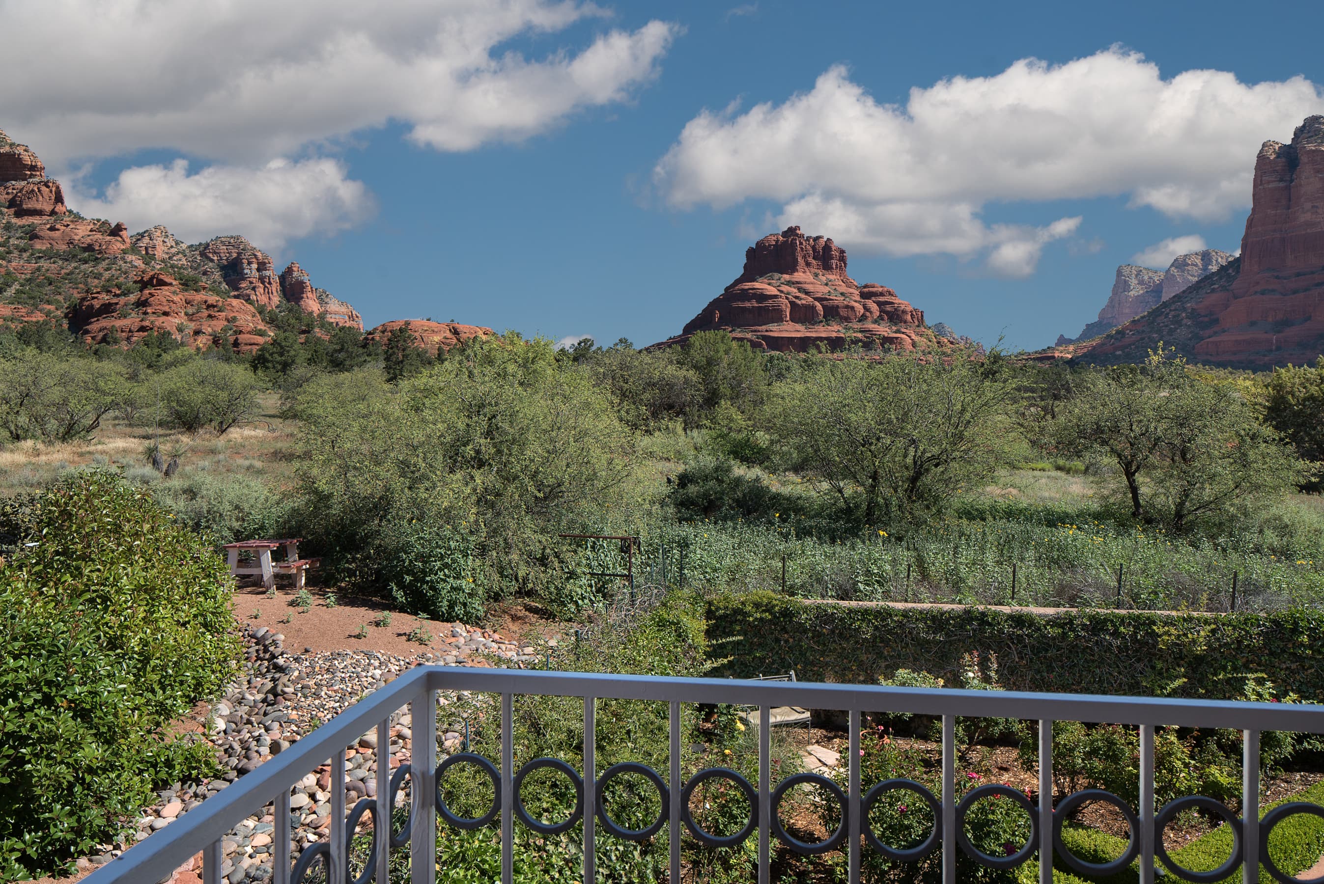 A stunning balcony view showcasing lush green landscape with distant red rock formations under a partly cloudy blue sky.
