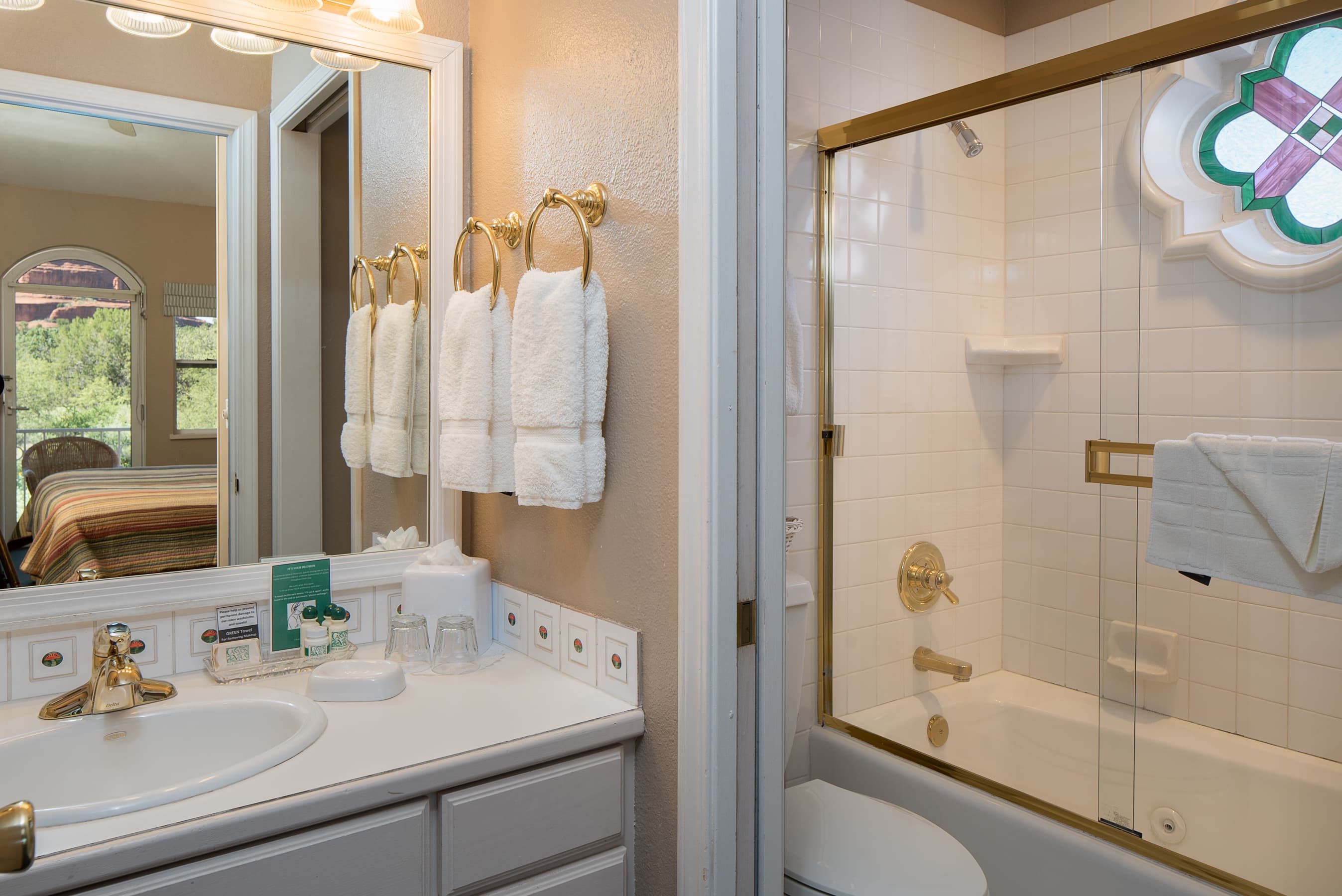 An elegant bathroom featuring a single vanity with a large mirror, a shower-tub combo with a glass door, and a decorative window.