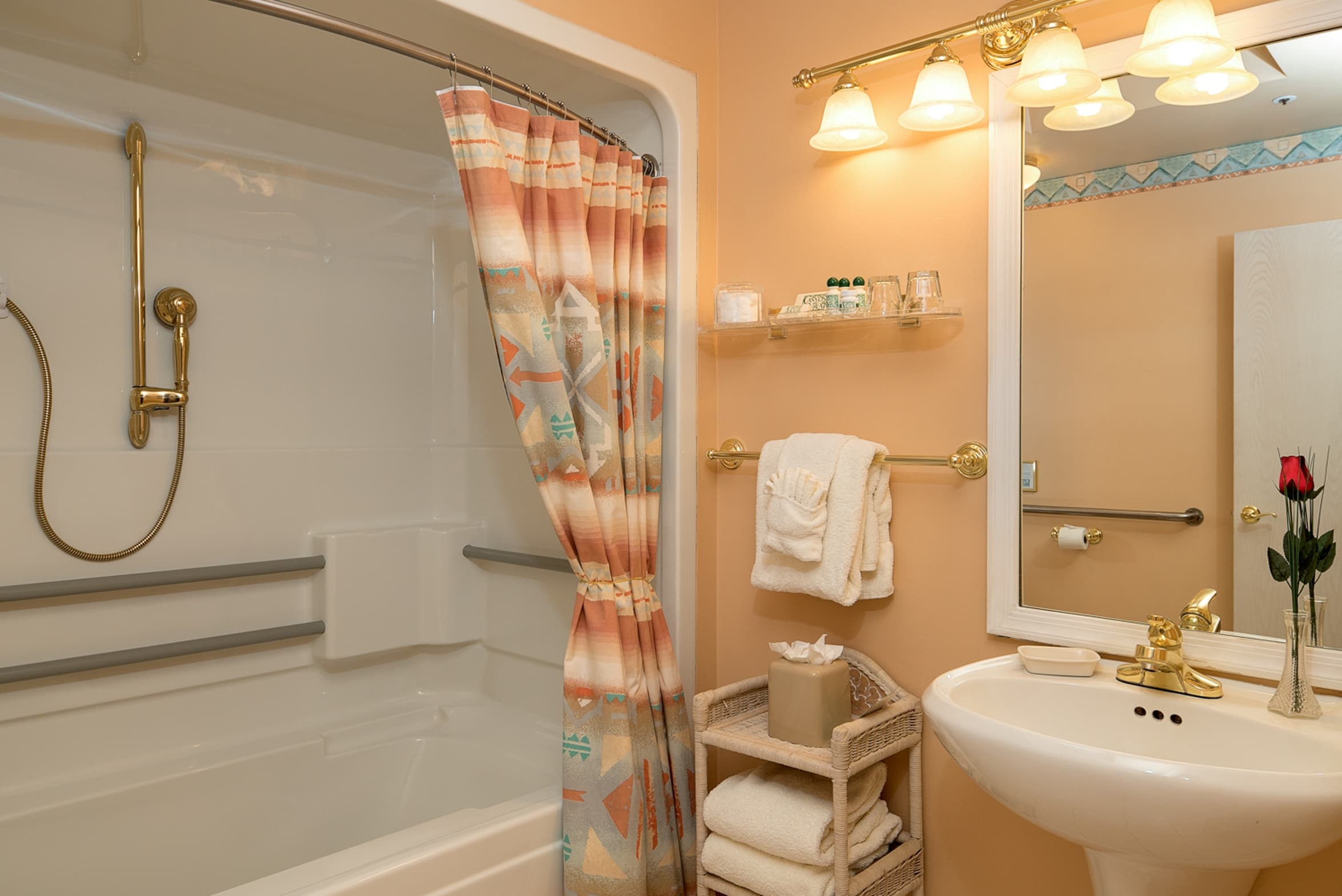 A bathroom with a white pedestal sink, a large mirror, and a shower-tub combo with and gold fixtures.