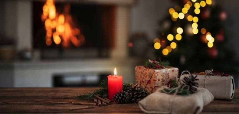 A cozy Christmas scene featuring a lit candle, wrapped gifts, and a warm fireplace.