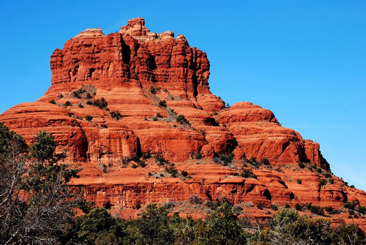 Red rock formation with layered cliffs under a clear blue sky.