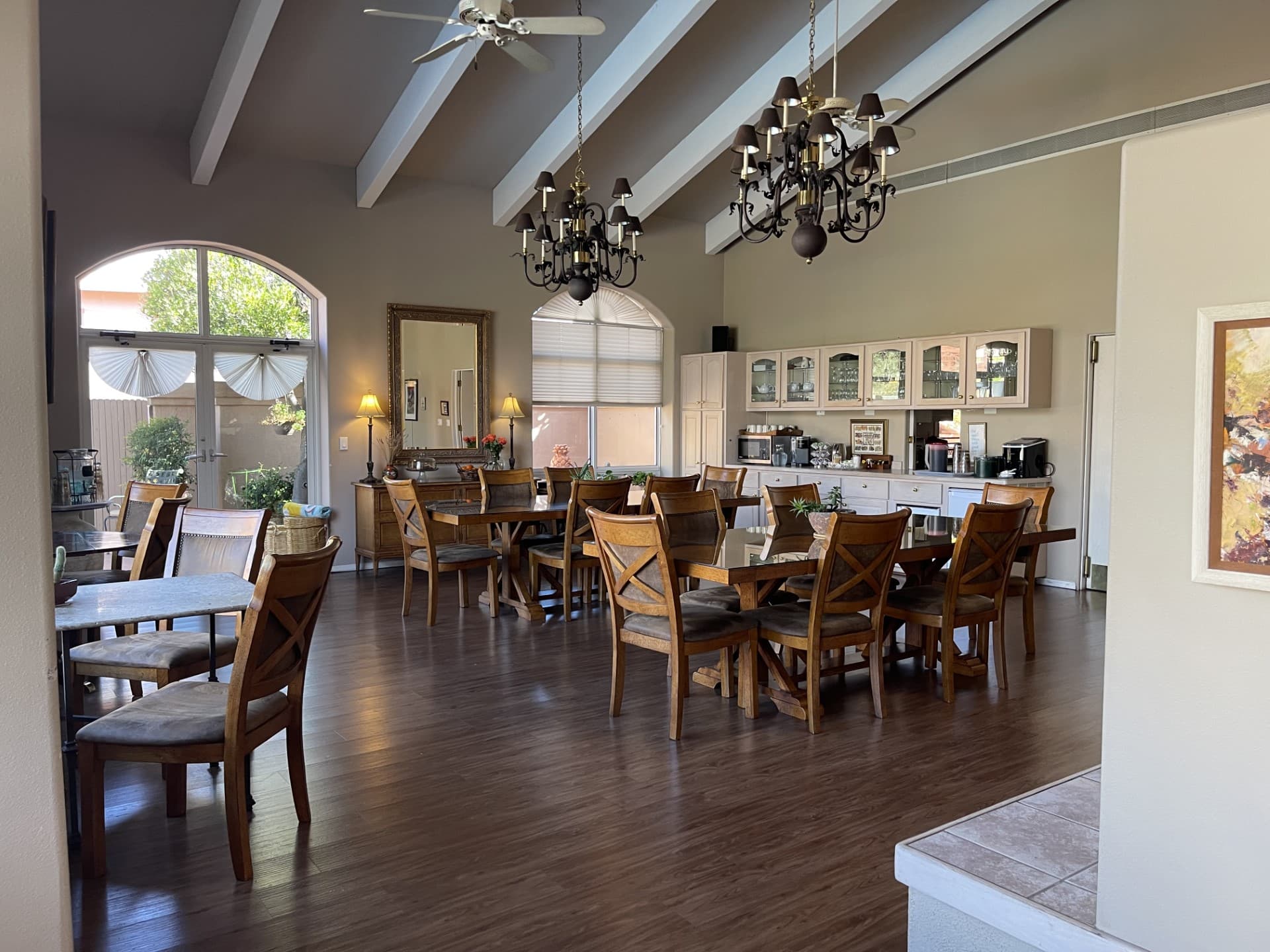 A spacious dining area with wooden tables and chairs, large windows, and a decorative chandelier.