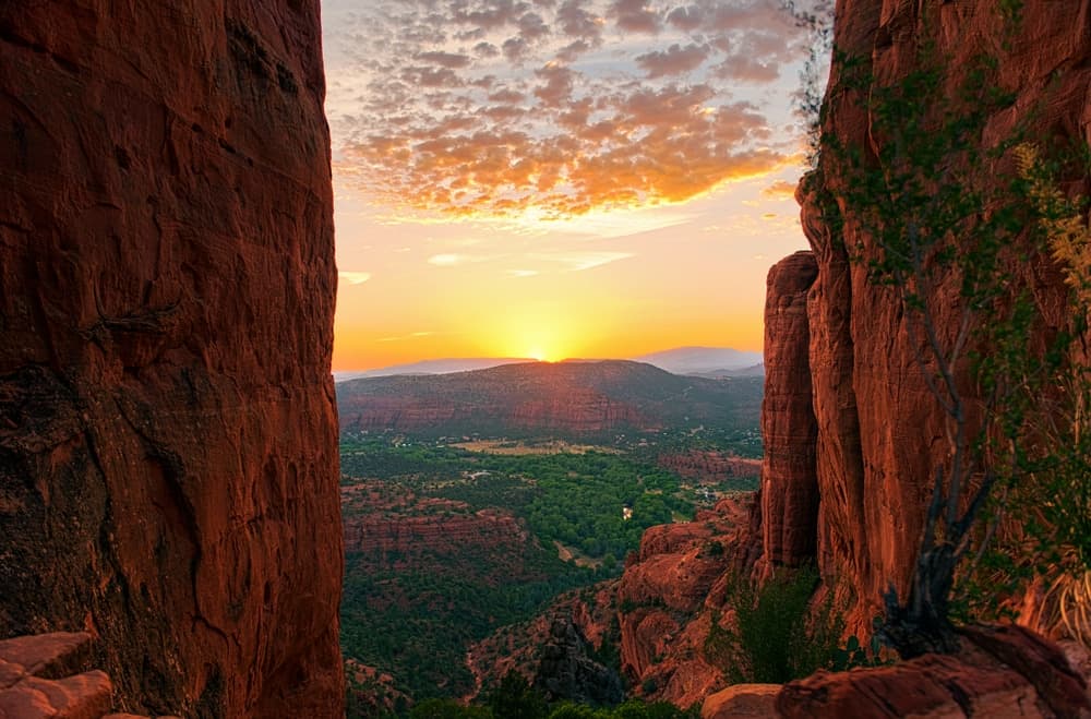 A sunset casts warm hues over a valley framed by red rock formations.