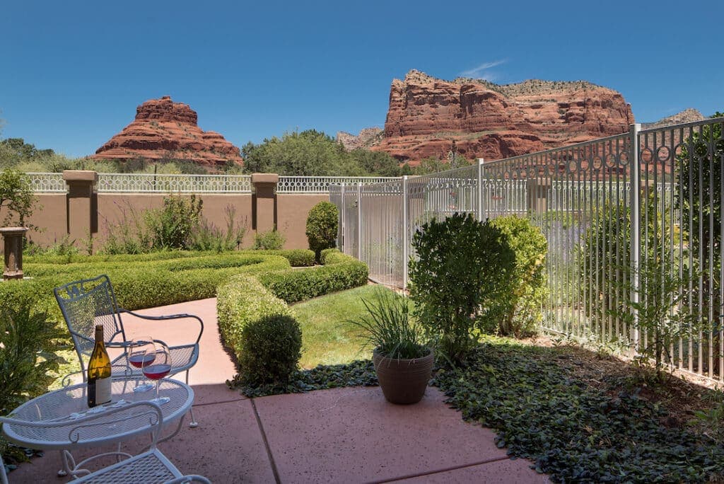 A serene outdoor patio with white furniture overlooks lush greenery and red rock formations under a clear blue sky.