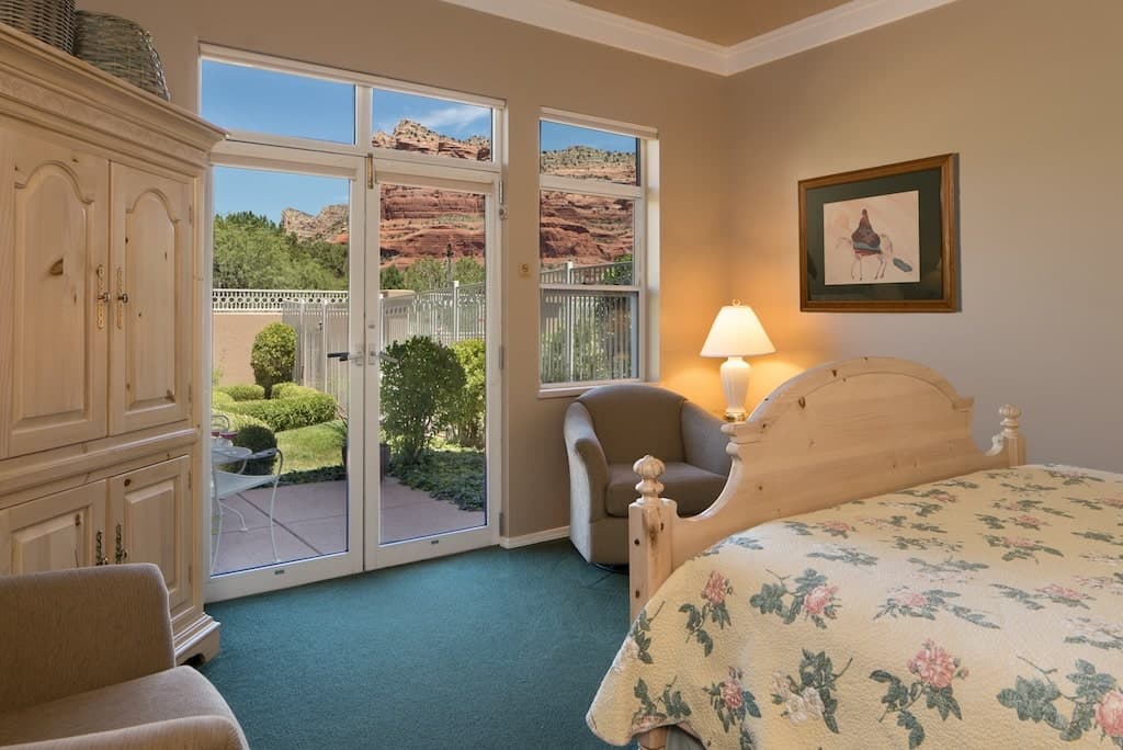 Cozy bedroom with a floral quilt, armchairs, and a view of red rock formations outside.