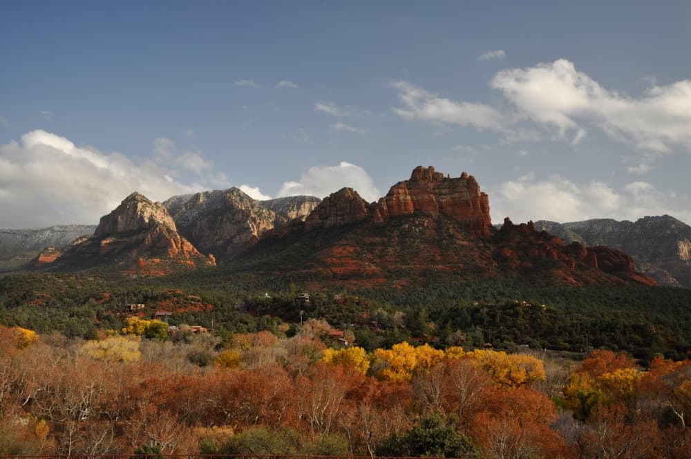 Vibrant autumn foliage foregrounds rugged red rock formations under a cloudy sky.