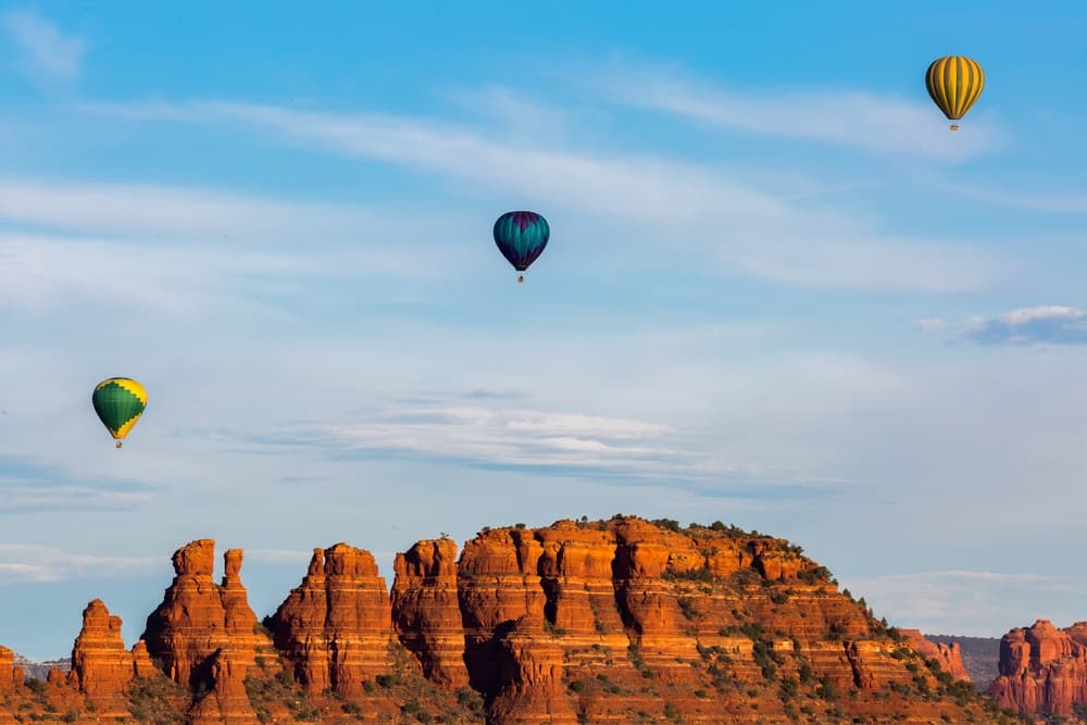 Three hot air balloons float above red rock formations under a blue sky.