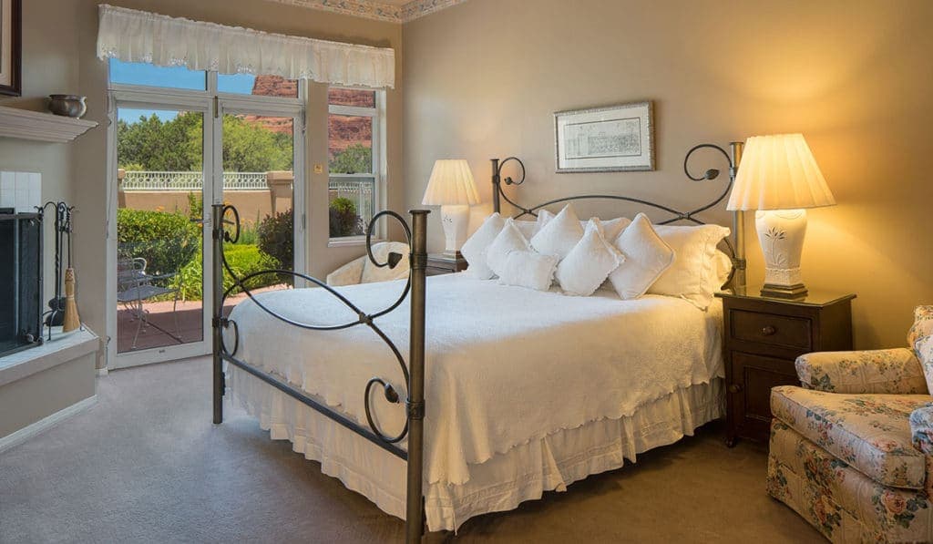 Cozy bedroom featuring a wrought-iron bed, soft white bedding, and large windows overlooking a garden.