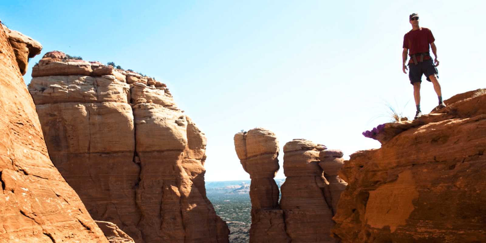 A hiker stands on the edge of a rocky cliff, overlooking a scenic landscape.