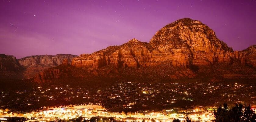A majestic mountain illuminated by a purple sky over a twinkling town at dusk.