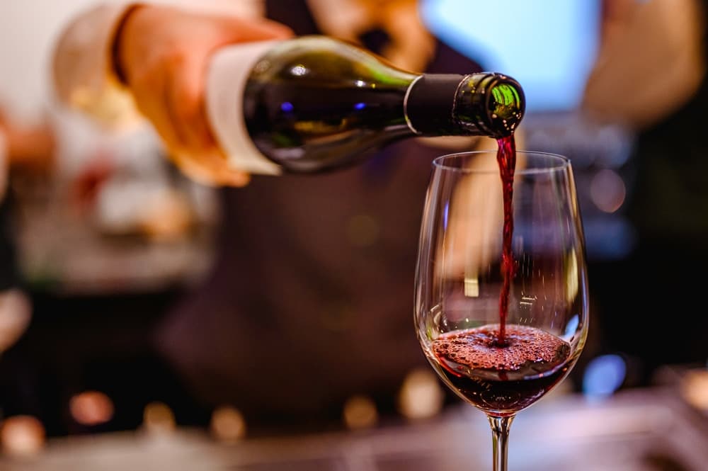 A close-up of a hand pouring red wine from a bottle into a glass.