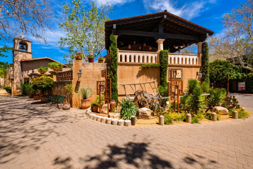 A charming courtyard featuring a rustic building with a wooden roof surrounded by greenery and decorative elements.