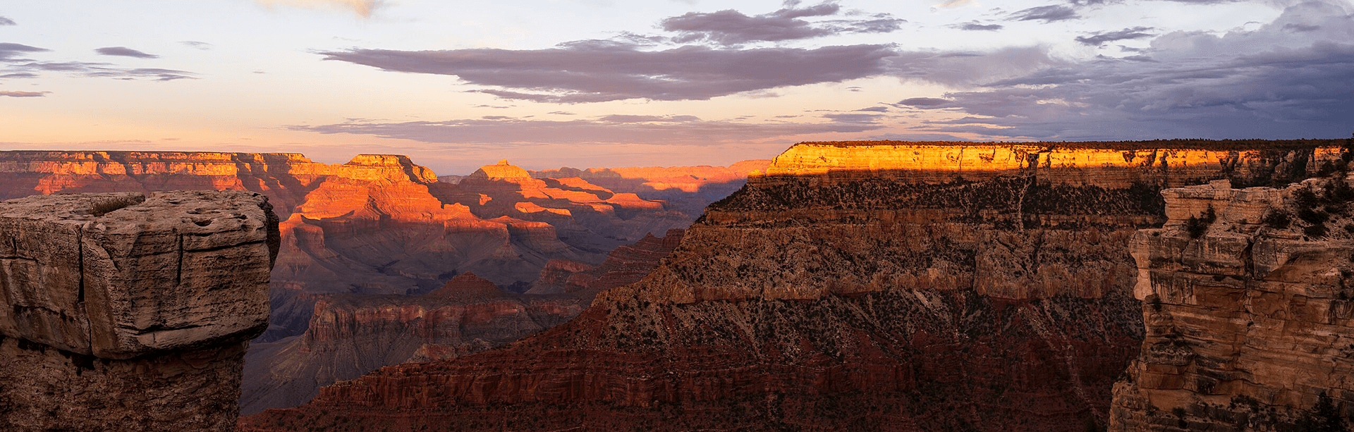 A stunning view of the Grand Canyon at sunset with layered rock formations illuminated by golden light.