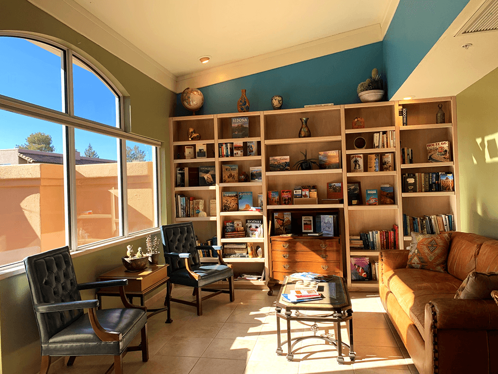 A cozy reading nook with a bookshelf, two chairs, a sofa, and large windows letting in natural light.