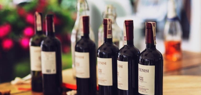 A row of wine bottles with red labels sitting on a wooden table, surrounded by greenery.