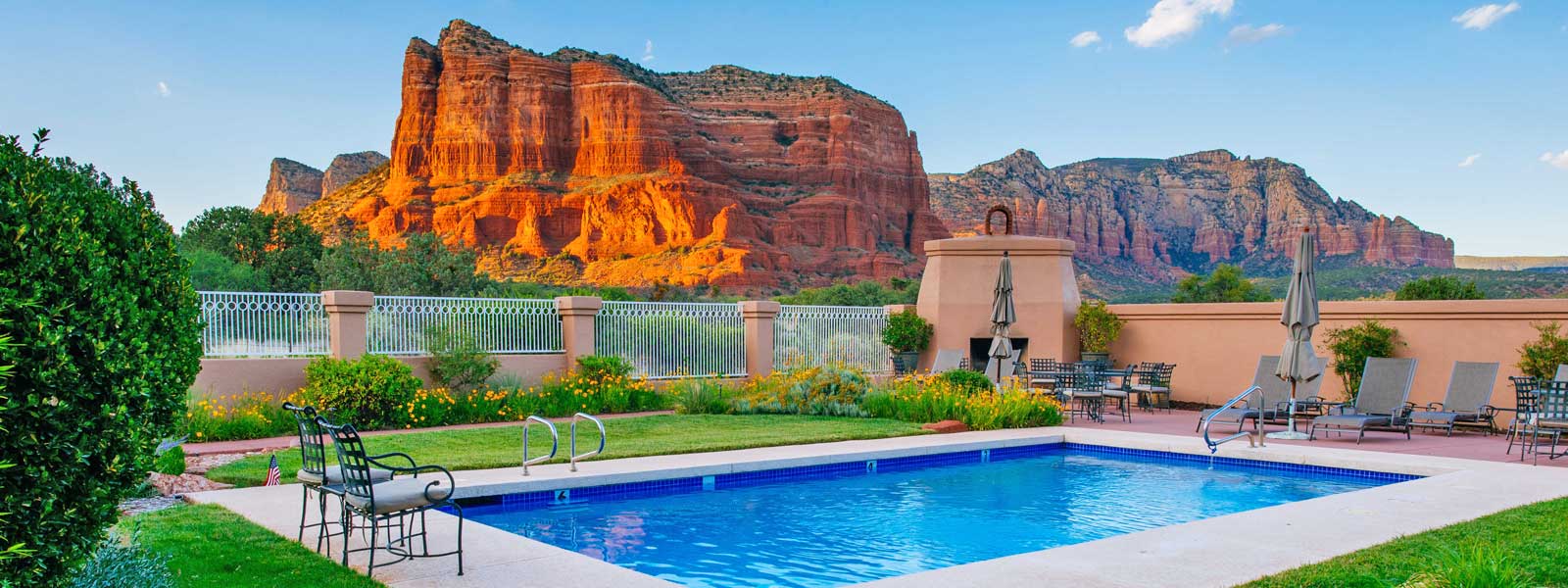 A serene backyard with a swimming pool, framed by vibrant red rock formations under a clear blue sky.