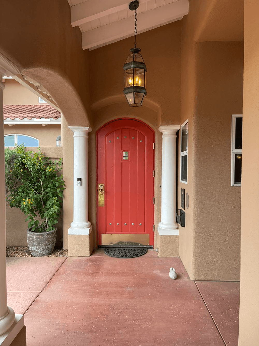 A welcoming entrance featuring a red door, hanging lantern, and potted plant.