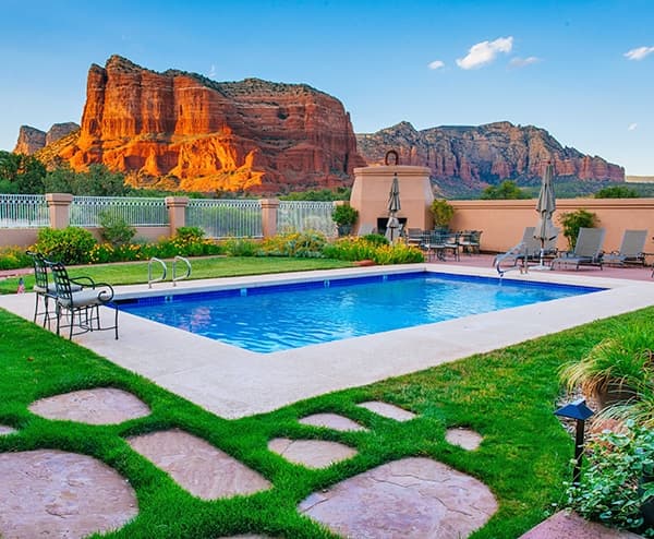 A serene pool surrounded by landscaped grass and rock formations under a clear blue sky.