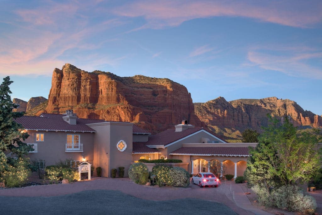 A picturesque home with a landscaped yard set against a backdrop of red rock formations at sunset.