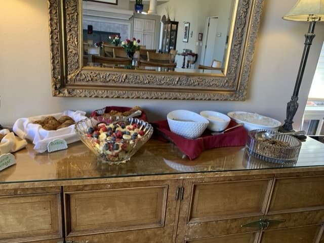 A buffet table displaying a fruit salad, cookies, and bowls of various dishes, all set within a warmly decorated dining area.