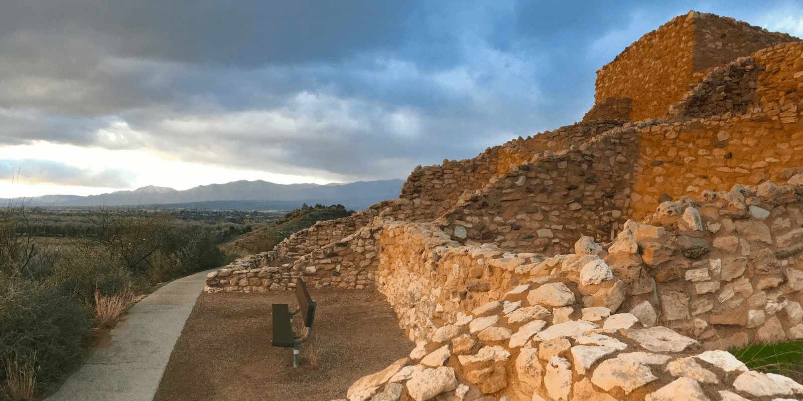 Ruins of a stone structure overlook a valley beneath a cloudy sky.