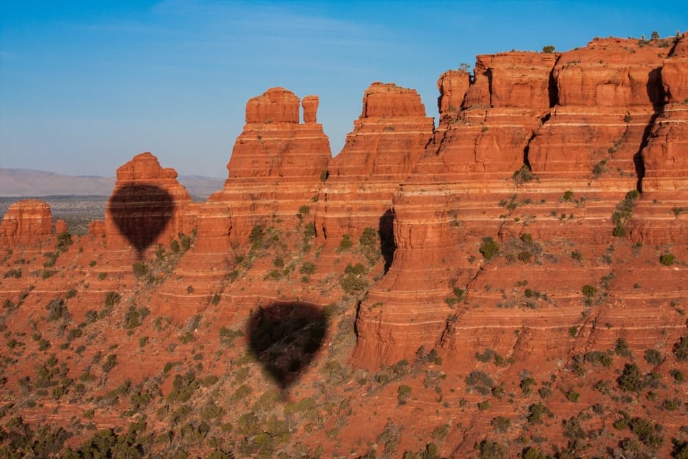Hot air balloon shadows cast on red rock formations under a clear blue sky.