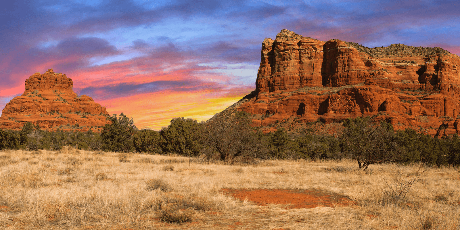 Panoramic view of red rock formations under a colorful sunset sky.