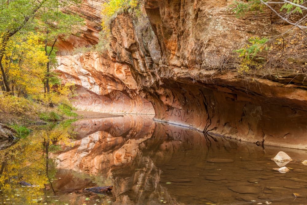 A serene canyon scene with autumn foliage reflected in calm waters.