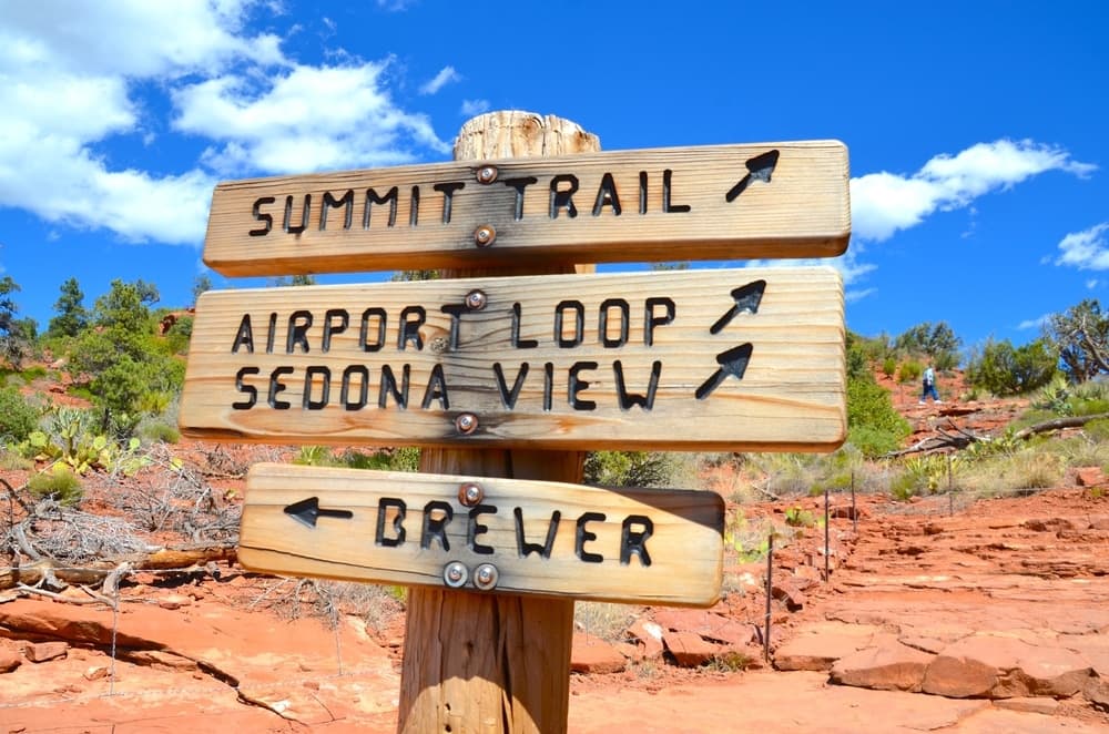 Wooden directional signs pointing to hiking trails: Summit Trail, Airport Loop, Sedona View, and Brewer.