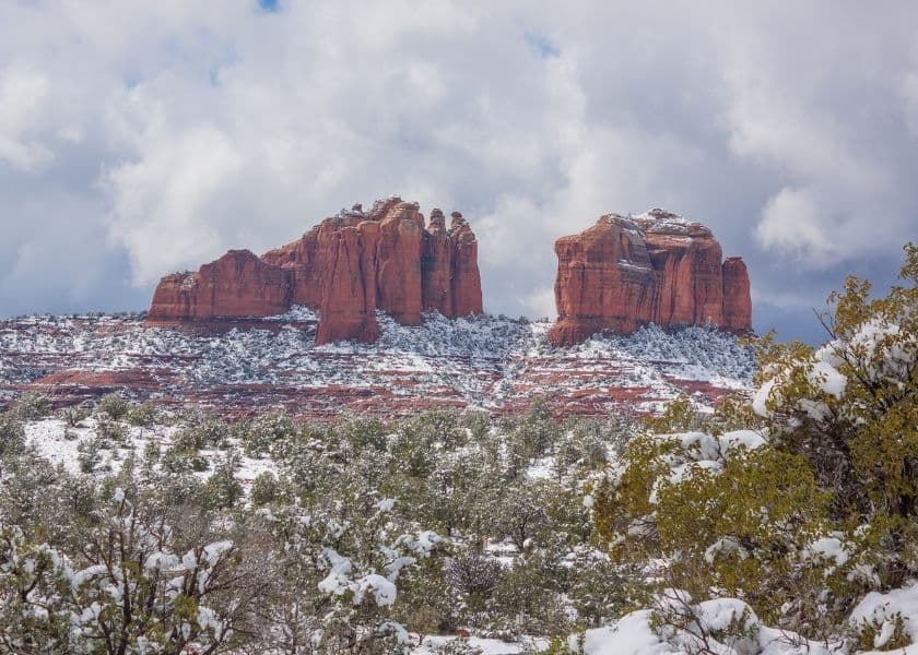 Red rock formations dusted with snow under a cloudy sky.