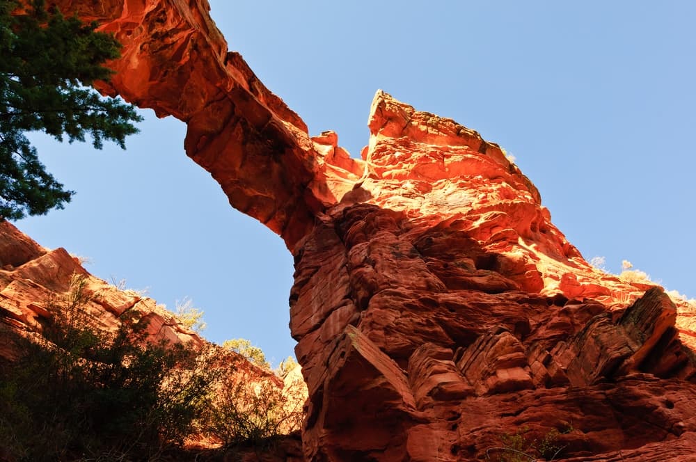 A towering red rock formation with an arch against a blue sky.