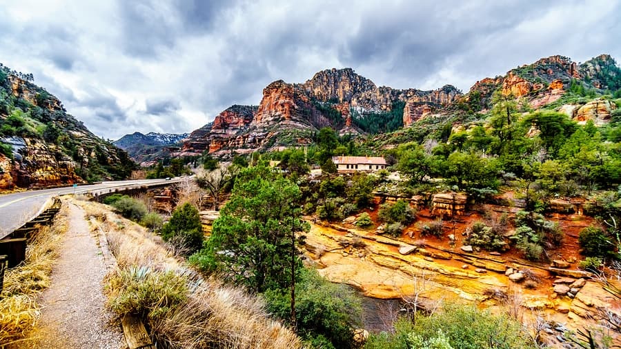 Scenic view of a winding road surrounded by red rock formations and lush greenery under a cloudy sky.