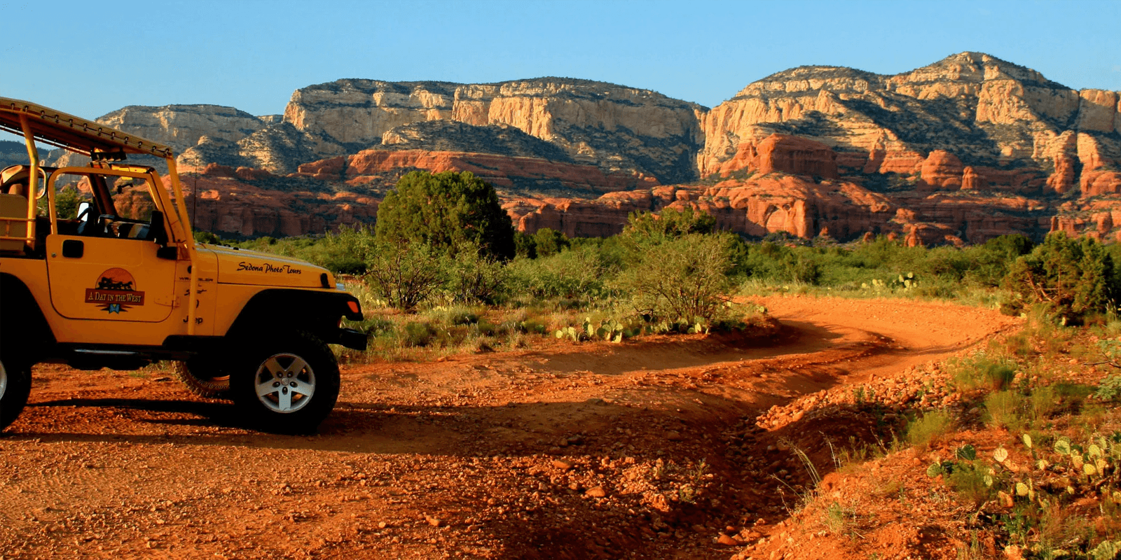 A yellow jeep parked on a dirt path with red rock formations in the background.
