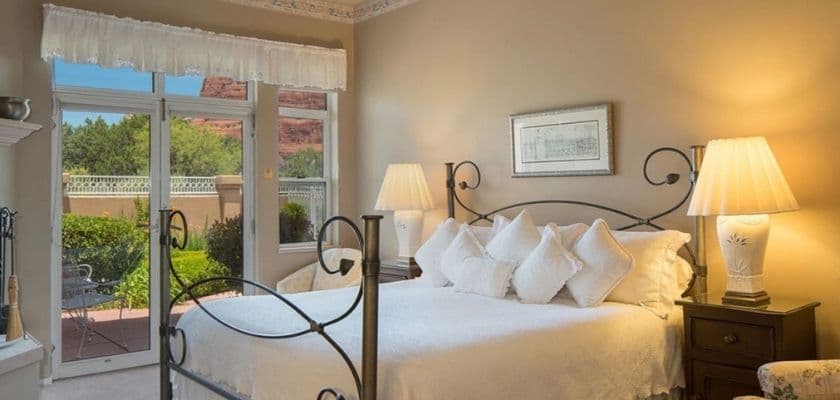 A cozy bedroom featuring a wrought-iron bed, dressed with white pillows, and large windows overlooking a garden.
