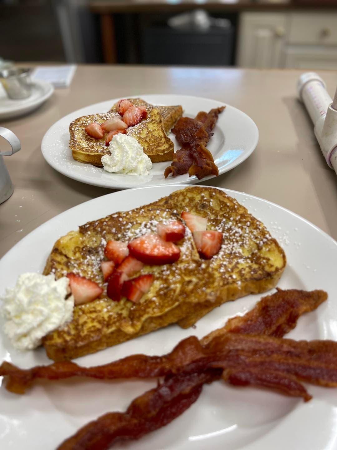 A plate of French toast topped with strawberries and whipped cream, accompanied by crispy bacon.
