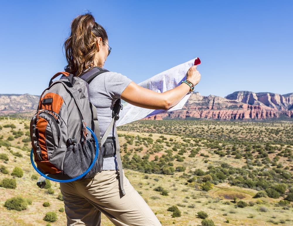 A hiker looks at a map while standing on a rocky overlook with a vast landscape in the background.