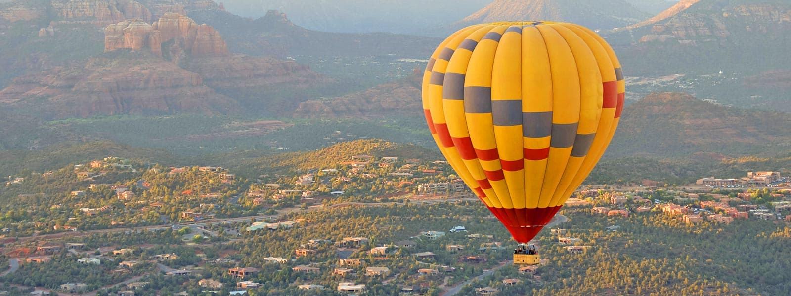 A vibrant yellow hot air balloon floats over a scenic landscape.