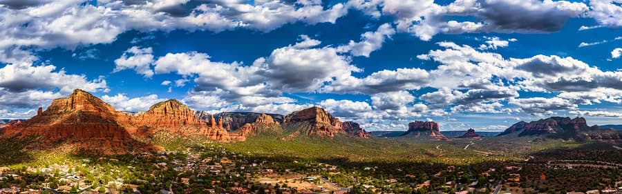 A panoramic view of rugged red mountains under a blue sky with fluffy white clouds.