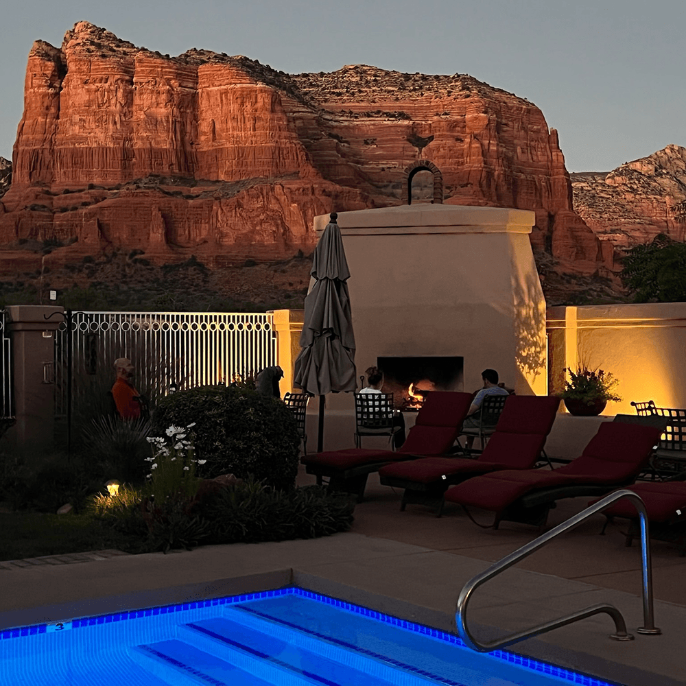Outdoor stone fireplace at near swimming pool at twilight with Sedona Arizona Red Rocks in the background