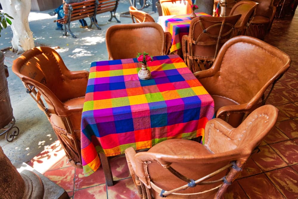 A colorful checkered tablecloth adorns a table surrounded by leather chairs in an outdoor café setting.