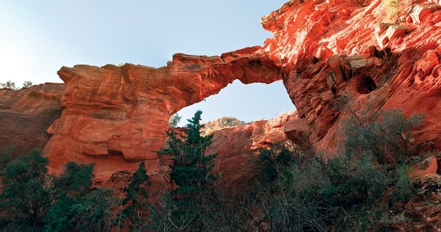Red rock formations create a natural arch against a clear blue sky.