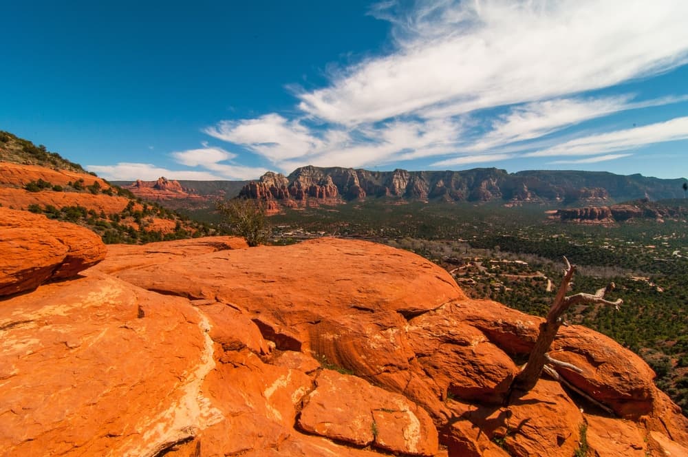 A panoramic view of red rock formations and hills under a blue sky with scattered clouds.
