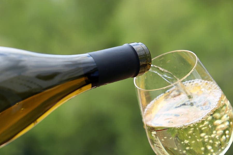A wine bottle is pouring into a glass against a blurred green background. A wine bottle is pouring into a glass against a blurred green background.