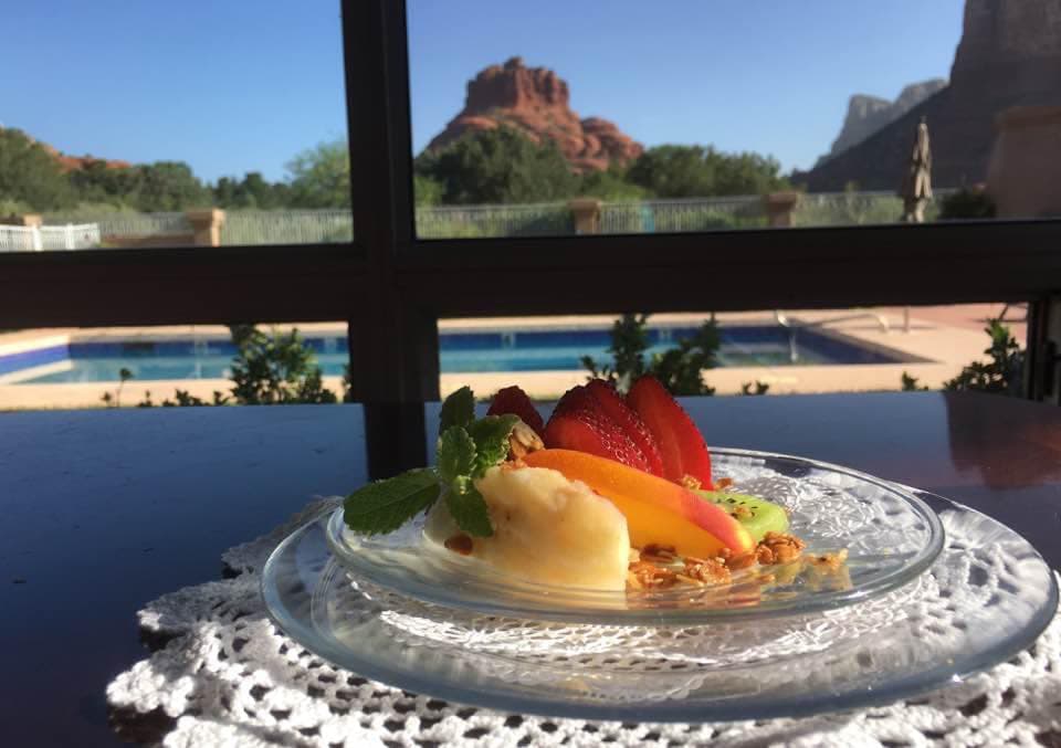 A colorful fruit dessert on a glass plate with a pool and mountains visible in the background.