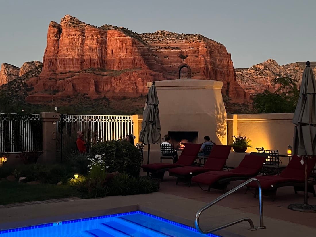 A serene outdoor space features a swimming pool, red rock formations in the background, and comfortable lounge chairs.