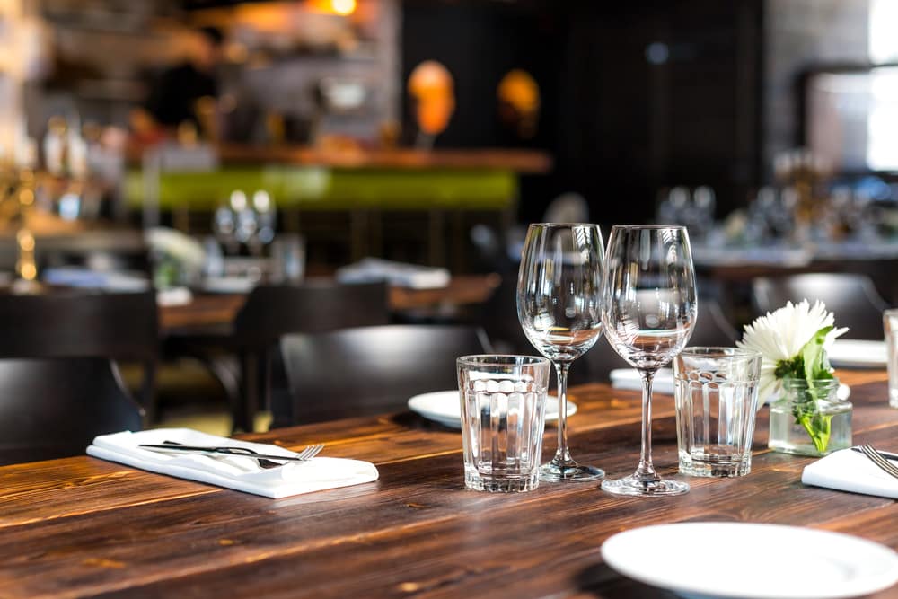 A table set for dining with wine glasses, water glasses, utensils, and a flower centerpiece in a restaurant.
