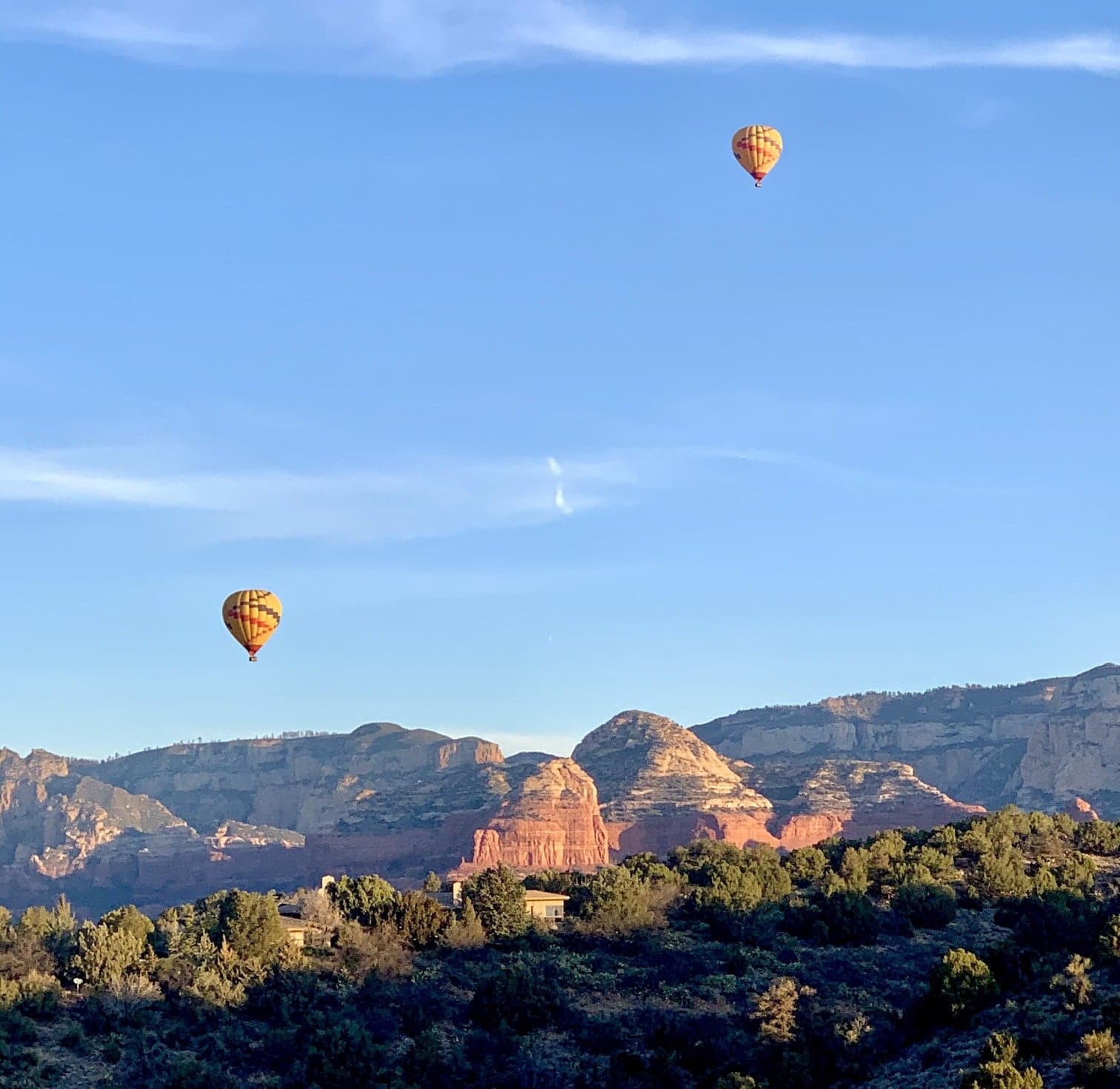 Two hot air balloons float above red rock formations under a clear blue sky.