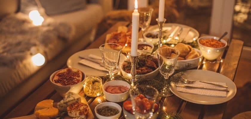 cozy holiday dinner table set with candles glassware festive lights and assorted dishes